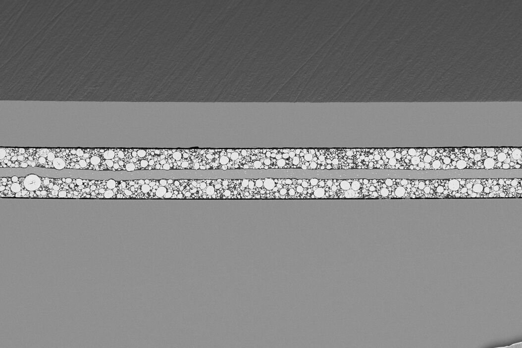 [Translate to German:] SEM image of the full Li-NMC electrode sample, showing the two porous layers and the metal film at the center of the structure. Cross_Section_Ion_Beam_Milling_of_Battery_Components_teaser.jpg