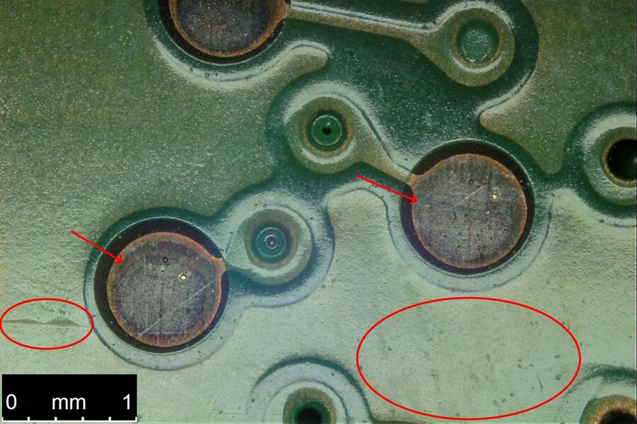 Image of the same portion of the PCB shown in Fig. 4a. The image was recorded with the DVM6 using integrated coaxial oblique illumination and 1/4 wave plate with relief contrast. Notice the scratches and defects on the pads (arrows) and imperfections and variations on the substrate (encircled areas) become more visible compared to the ring light illumination (Fig. 4a).