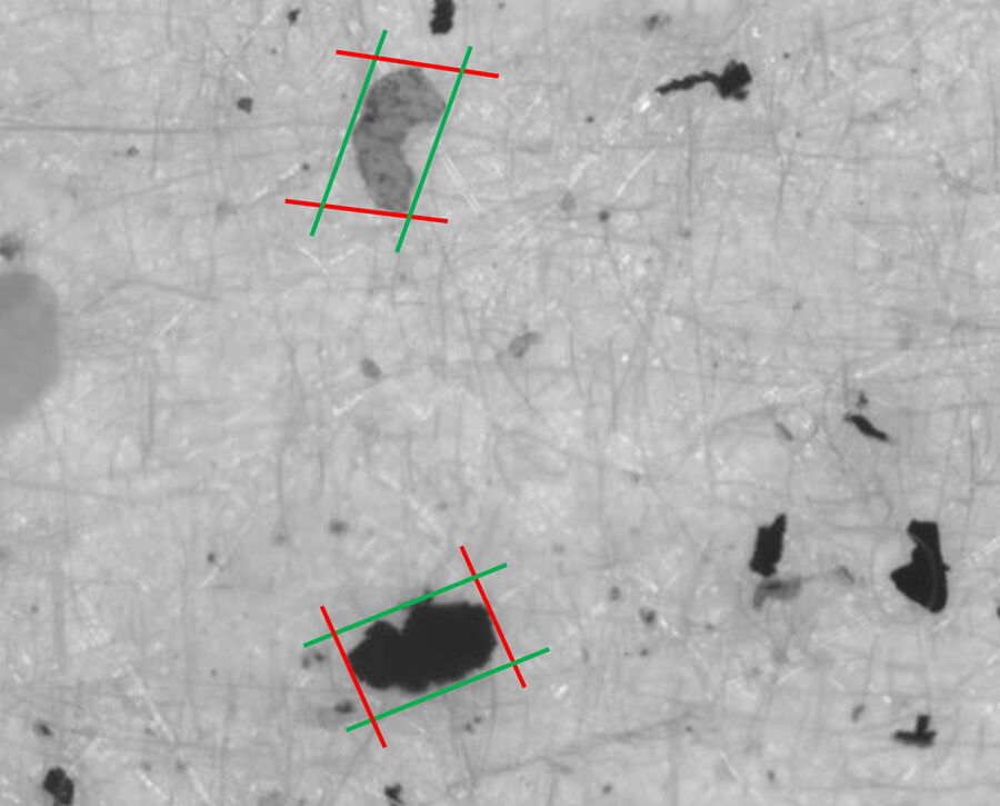 Image of particles on a filter. The particles can have unusual shapes. The red lines indicate the max Feret diameter and the green ones the min Feret diameter of the 2 particles marked.