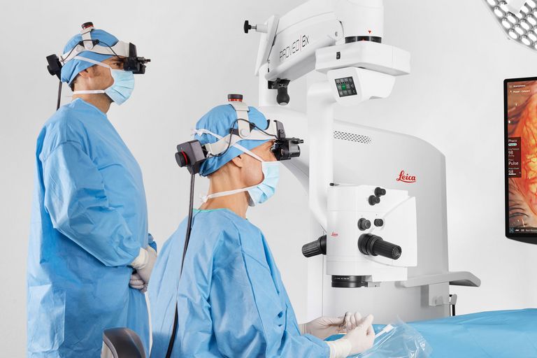 A surgeon and resident using MyVeo headsets for shared 3D visualization during ophthalmic surgery.